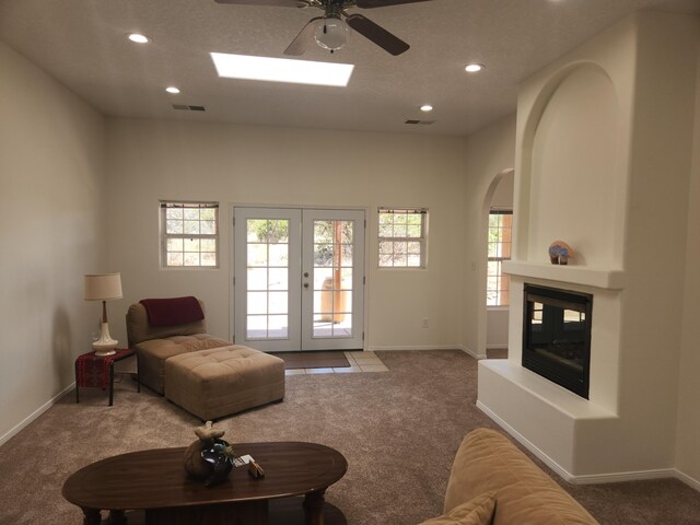 living room with ceiling fan, light carpet, a fireplace, and a skylight