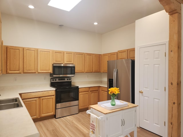 kitchen featuring stainless steel appliances, a skylight, sink, and light hardwood / wood-style flooring