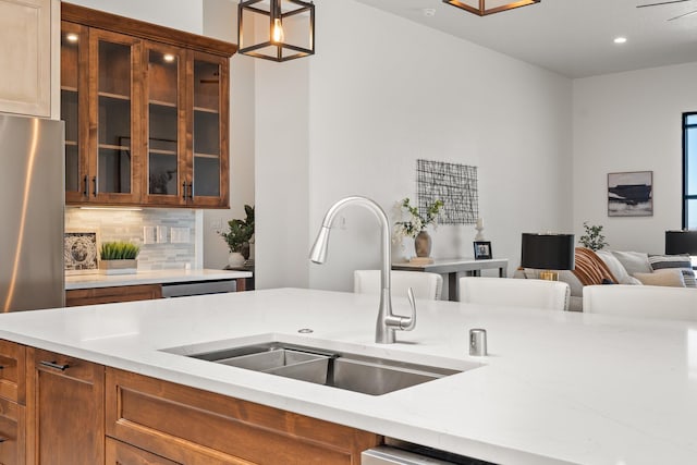 kitchen with pendant lighting, backsplash, sink, stainless steel fridge, and light stone countertops