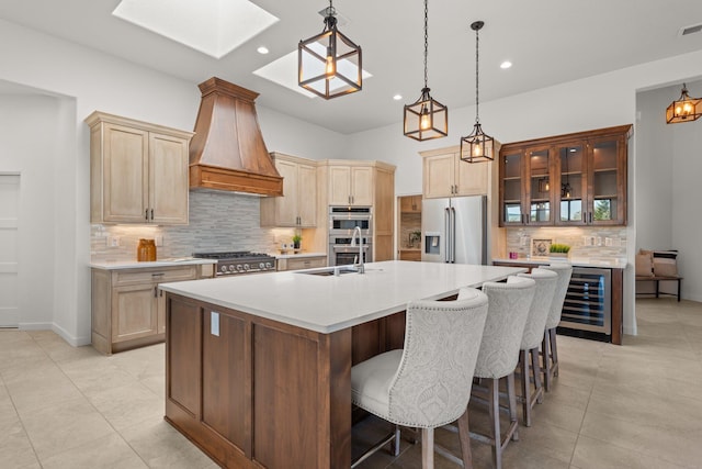 kitchen with decorative backsplash, custom exhaust hood, stainless steel appliances, beverage cooler, and an island with sink