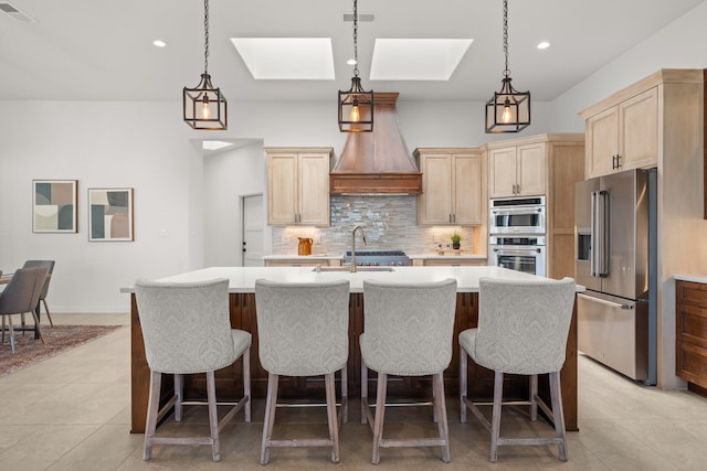 kitchen with a skylight, stainless steel appliances, tasteful backsplash, pendant lighting, and a center island with sink