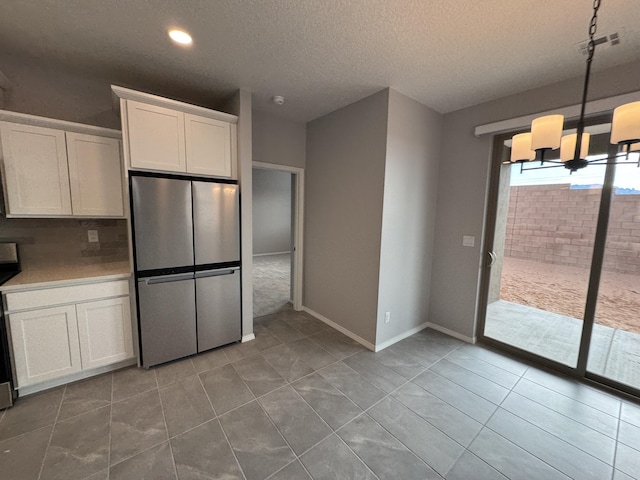 kitchen featuring white cabinets, tile patterned floors, stainless steel fridge, a textured ceiling, and a notable chandelier