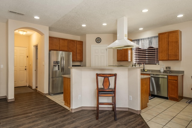 kitchen with light wood-type flooring, a kitchen island, island exhaust hood, a textured ceiling, and stainless steel appliances