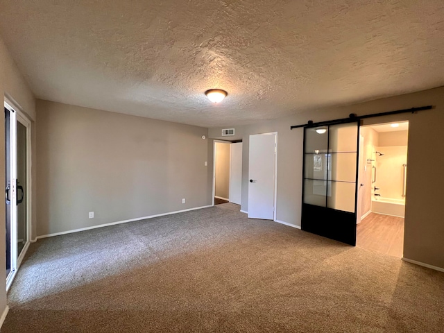 empty room featuring a textured ceiling, a barn door, and carpet floors