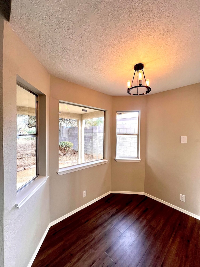 unfurnished room featuring an inviting chandelier, a textured ceiling, wood-type flooring, and a wealth of natural light