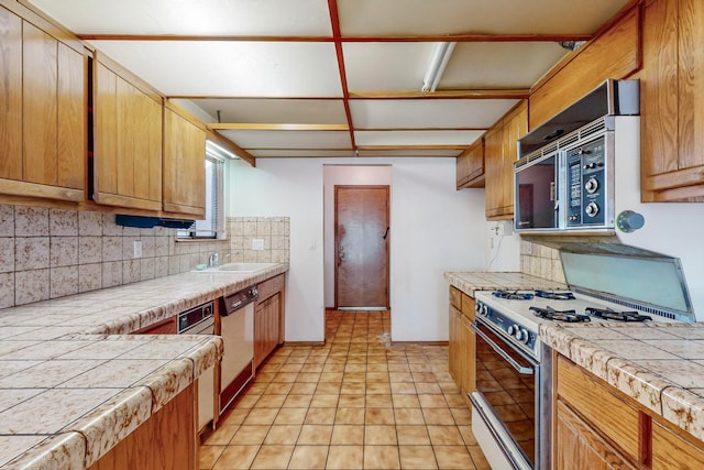 kitchen with sink, white gas range oven, backsplash, stainless steel dishwasher, and tile counters