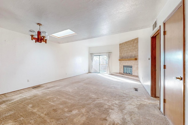 unfurnished living room featuring light colored carpet, a textured ceiling, a chandelier, a tile fireplace, and a skylight