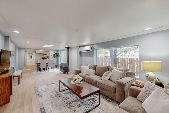 living room with a wall unit AC, a skylight, and light wood-type flooring