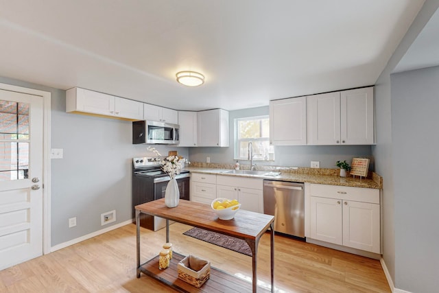 kitchen with light stone countertops, sink, light wood-type flooring, white cabinetry, and stainless steel appliances