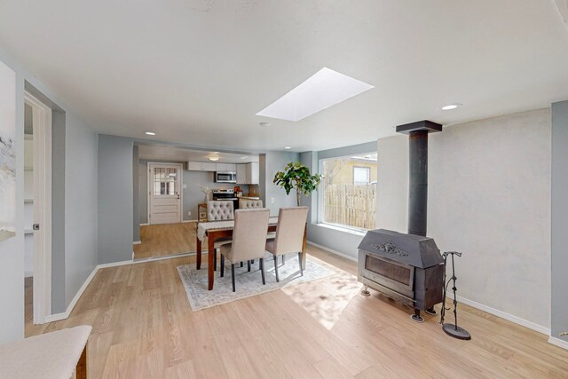 dining room featuring light hardwood / wood-style floors, a wood stove, and a skylight