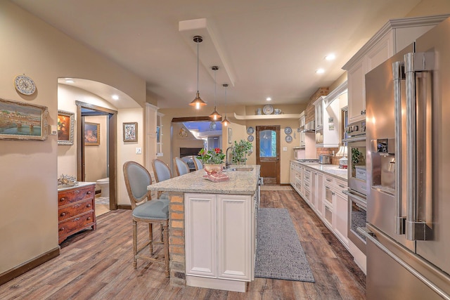 kitchen featuring pendant lighting, an island with sink, appliances with stainless steel finishes, light stone counters, and white cabinetry