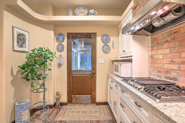 kitchen with white cabinets, light stone counters, stainless steel gas stovetop, and wall chimney range hood