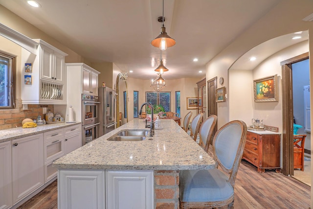 kitchen with sink, hanging light fixtures, an island with sink, white cabinetry, and stainless steel appliances