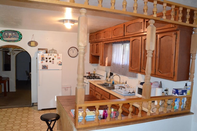 kitchen featuring arched walkways, white appliances, a sink, and brown cabinets