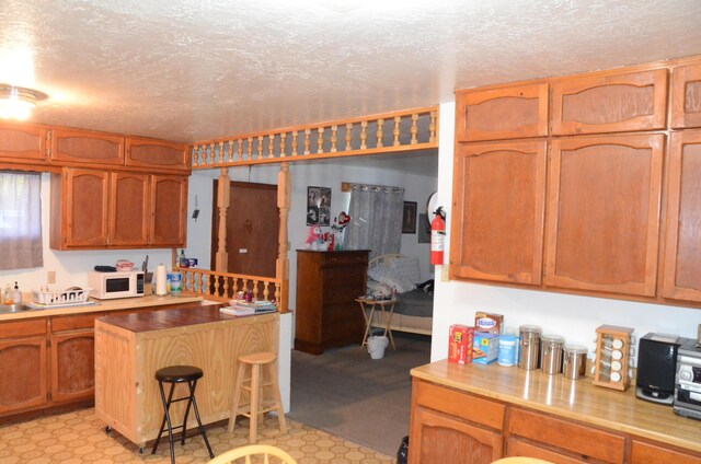 kitchen featuring light countertops, a textured ceiling, a breakfast bar area, and white microwave