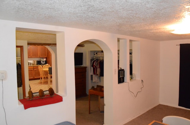 hallway with a textured ceiling, arched walkways, and carpet flooring