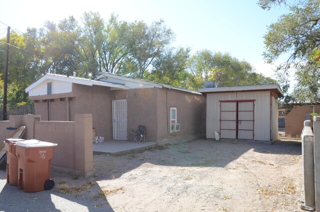 rear view of property featuring an outbuilding, a patio, dirt driveway, stucco siding, and a storage unit