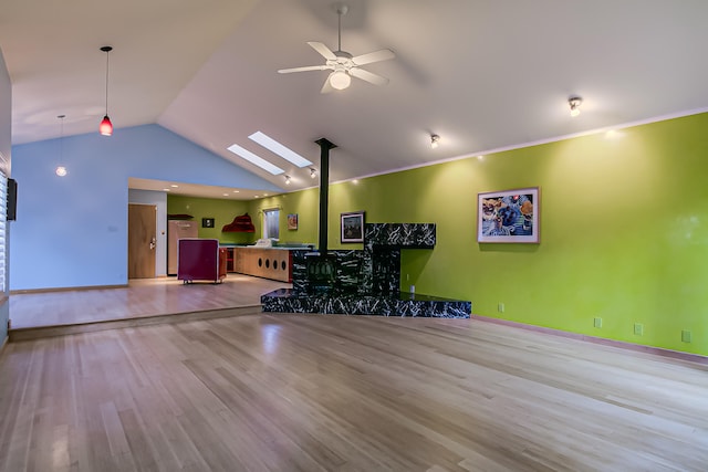 unfurnished living room featuring a wood stove, light hardwood / wood-style flooring, lofted ceiling with skylight, and ceiling fan