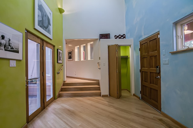 entryway with plenty of natural light, a towering ceiling, and light hardwood / wood-style flooring