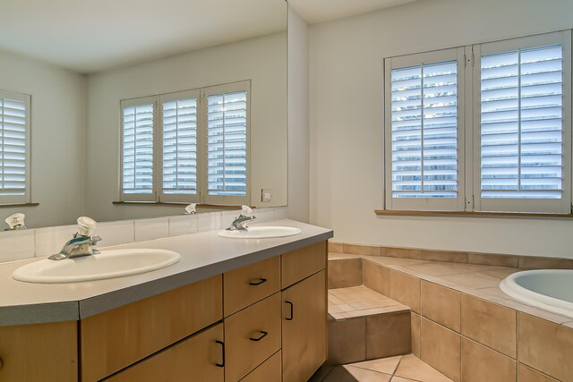 bathroom featuring tile patterned flooring, vanity, and tiled bath