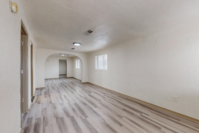 empty room with a textured ceiling and light hardwood / wood-style flooring