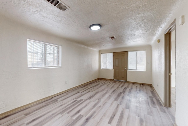 empty room featuring a healthy amount of sunlight, light hardwood / wood-style floors, and a textured ceiling