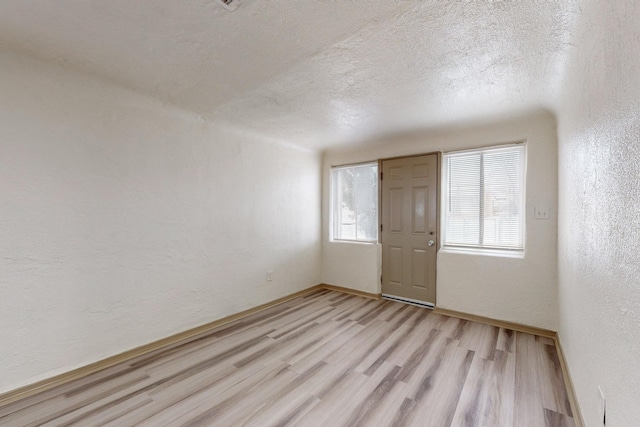 unfurnished room featuring a healthy amount of sunlight, a textured ceiling, and light wood-type flooring