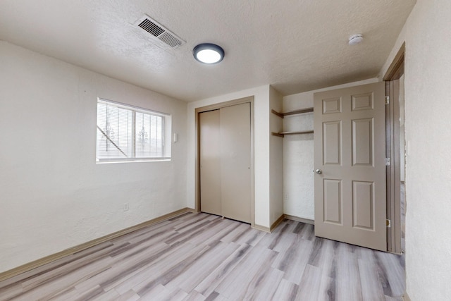 unfurnished bedroom featuring a closet, a textured ceiling, and light hardwood / wood-style flooring