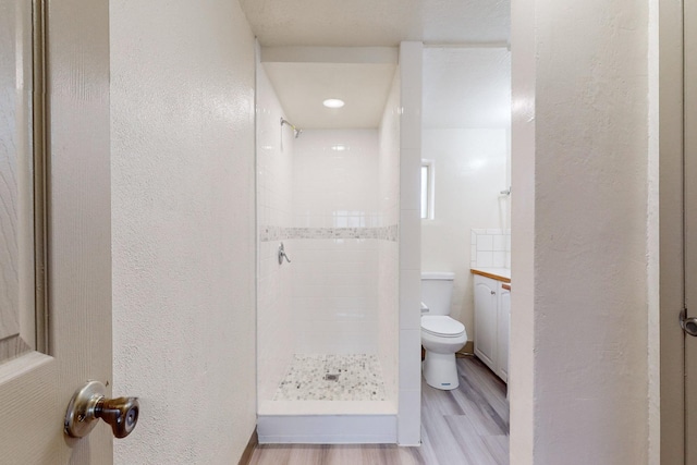 bathroom with toilet, a tile shower, and wood-type flooring