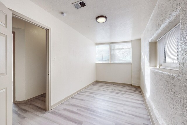 spare room with a textured ceiling and light hardwood / wood-style floors