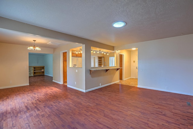 unfurnished living room featuring sink, wood-type flooring, a textured ceiling, and a chandelier