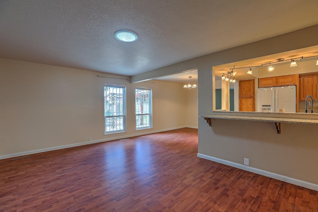 spare room featuring sink, a textured ceiling, a notable chandelier, and dark wood-type flooring