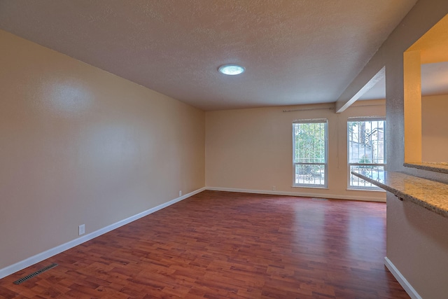 unfurnished living room featuring dark hardwood / wood-style flooring, a textured ceiling, and beamed ceiling