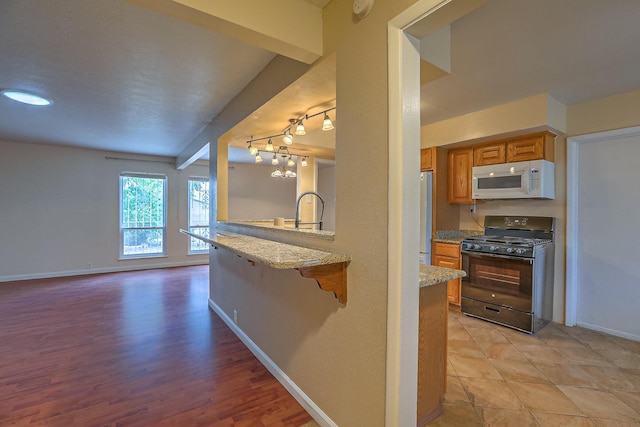 kitchen with black gas range, a breakfast bar area, kitchen peninsula, light stone countertops, and refrigerator