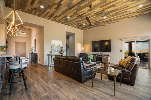 living room featuring ceiling fan with notable chandelier, hardwood / wood-style flooring, a towering ceiling, and wooden ceiling