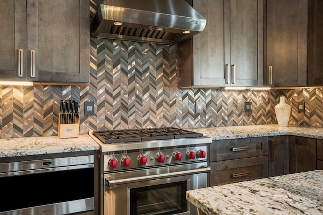 kitchen with light stone counters, stainless steel appliances, wall chimney range hood, and dark brown cabinetry