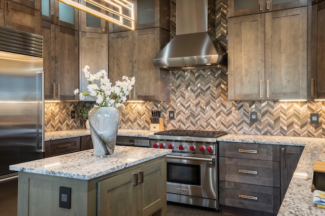 kitchen with light stone counters, premium appliances, wall chimney range hood, and decorative backsplash