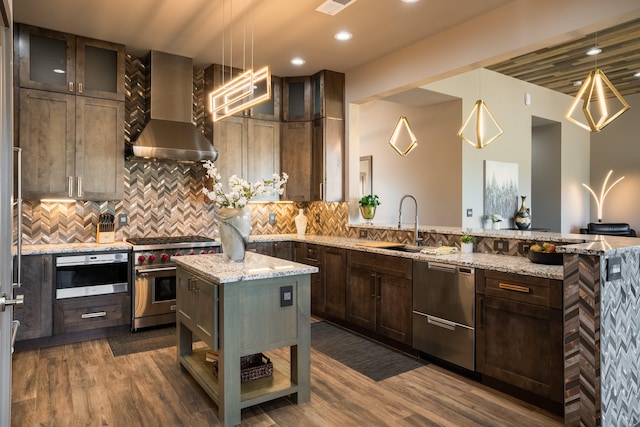 kitchen with hanging light fixtures, a kitchen island, appliances with stainless steel finishes, and wall chimney range hood