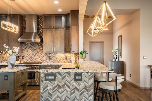 kitchen featuring wall chimney exhaust hood, designer range, light stone countertops, and pendant lighting