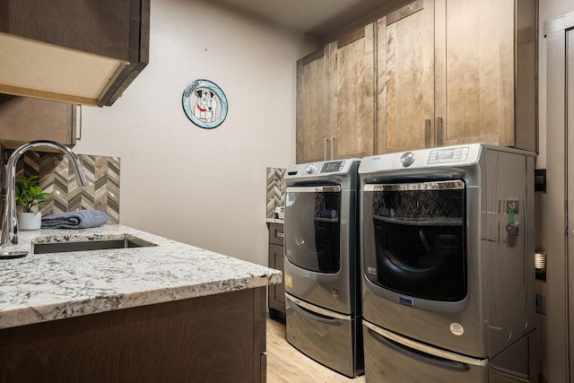 laundry room with sink, washing machine and dryer, light hardwood / wood-style floors, and cabinets