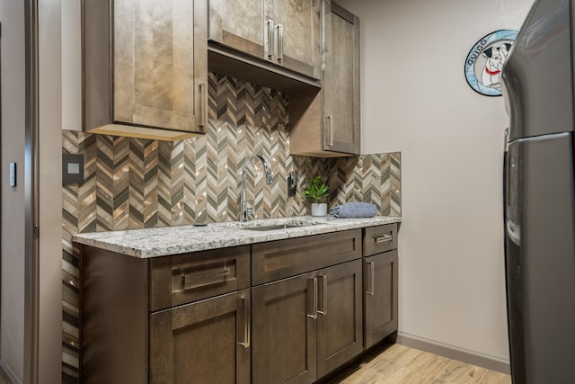 kitchen with light stone countertops, sink, light wood-type flooring, and stainless steel refrigerator