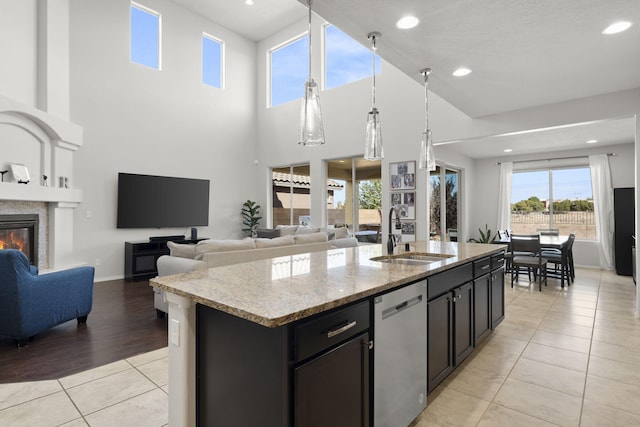 kitchen featuring light stone countertops, sink, light hardwood / wood-style floors, stainless steel dishwasher, and a center island with sink