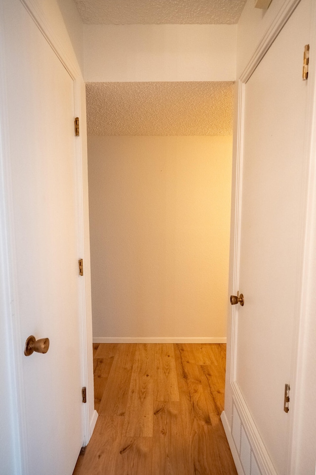 hallway with light hardwood / wood-style flooring and a textured ceiling