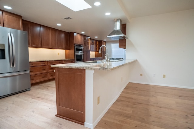 kitchen with kitchen peninsula, light wood-type flooring, stainless steel appliances, and wall chimney exhaust hood