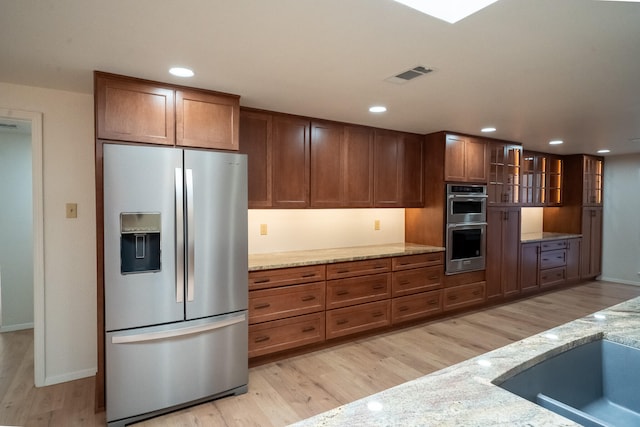 kitchen featuring appliances with stainless steel finishes, light wood-type flooring, light stone counters, and sink