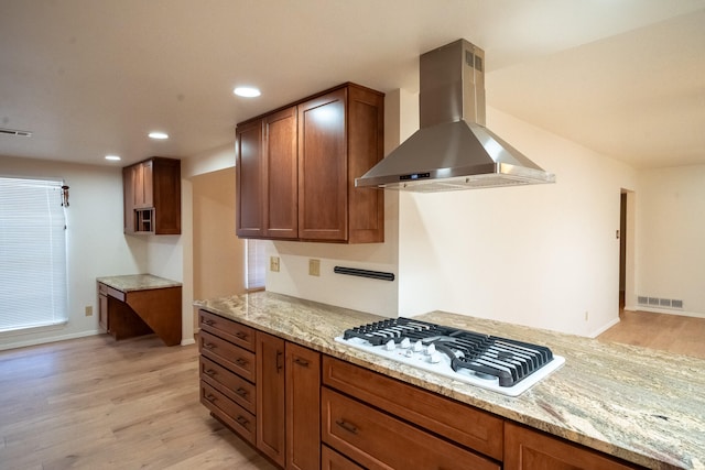 kitchen with white gas stovetop, wall chimney exhaust hood, light stone counters, and light wood-type flooring