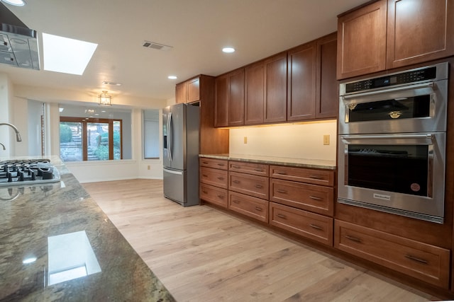 kitchen featuring a skylight, light stone countertops, light hardwood / wood-style floors, and appliances with stainless steel finishes