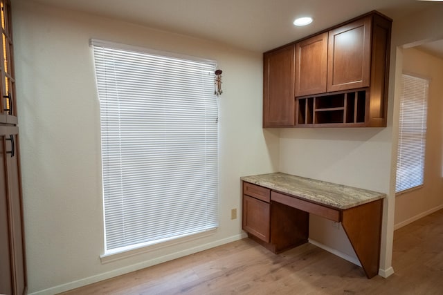 kitchen with light wood-type flooring, built in desk, and light stone counters