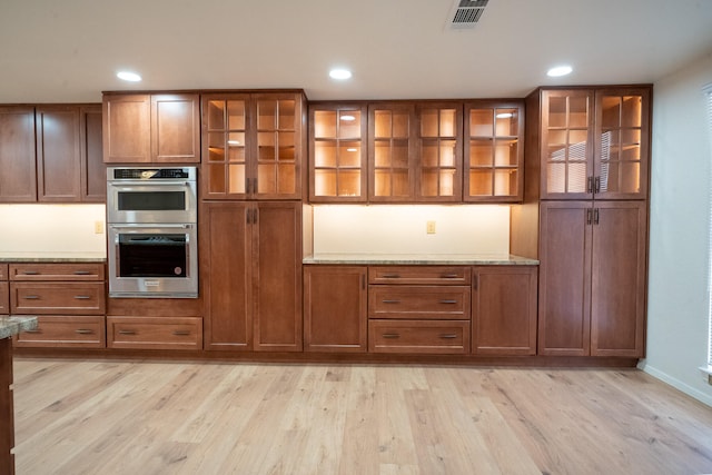 bar featuring light wood-type flooring, light stone counters, and double oven