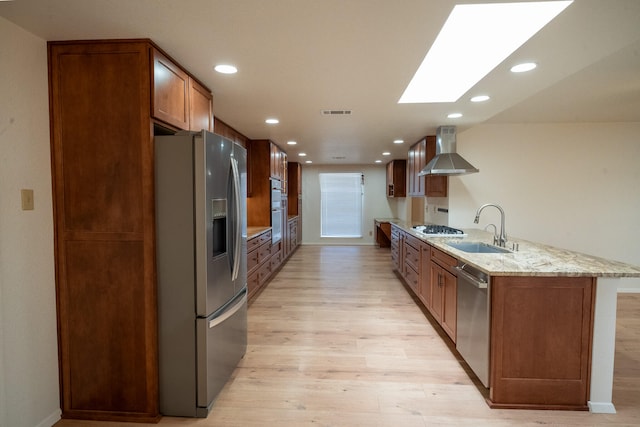 kitchen featuring sink, light hardwood / wood-style flooring, wall chimney exhaust hood, light stone counters, and stainless steel appliances